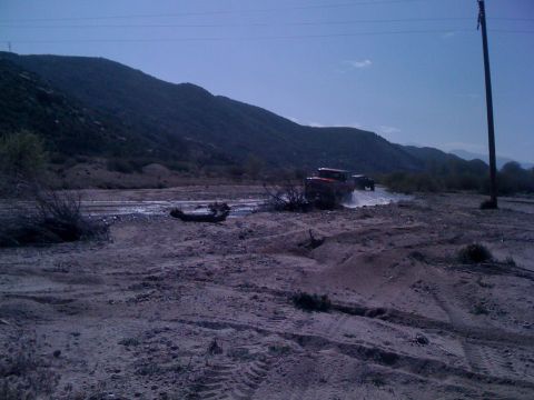1978 Ford Bronco - Two SUVs, including a 1978 Ford Bronco, navigate a dry riverbed under a clear blue sky.