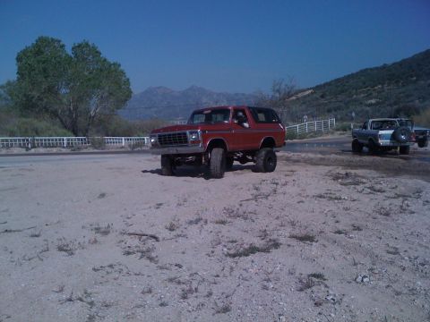 1978 Ford Bronco - A lifted 1978 Ford Bronco sits on a dirt lot with mountains in the distance and another truck nearby.