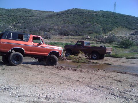 1978 Ford Bronco - Two Ford trucks, an orange Bronco and a brown pickup, are parked off-road in a dry, hilly landscape.