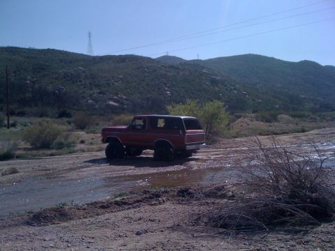 1978 Ford Bronco - A red 1978 Ford Bronco navigates a water crossing in a , outdoor setting.