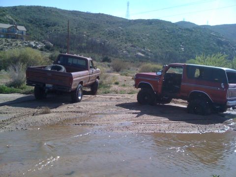 1978 Ford Bronco - Two trucks, a Ford Bronco and a pickup, are parked in a muddy, outdoor area.
