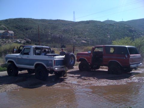 1978 Ford Bronco - Two Ford Broncos are parked in a muddy, off-road environment under a clear sky.