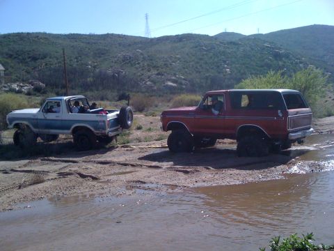 1978 Ford Bronco - Two Ford Broncos, one red and one blue and white, navigate a muddy off-road course.