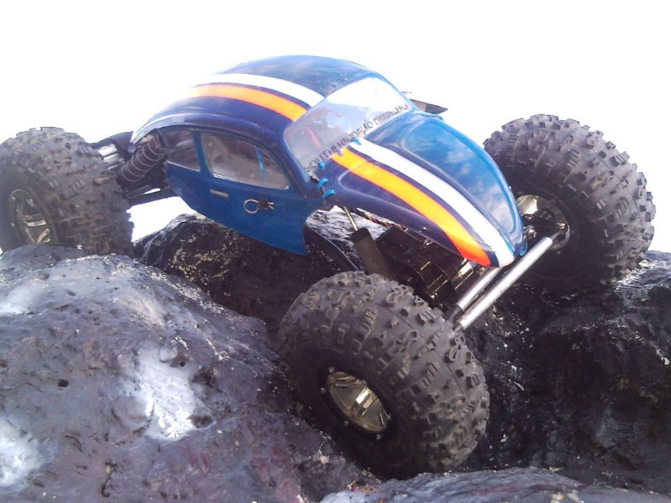 Blue remote control rock crawler with orange and white stripes on its body, climbing over rocks