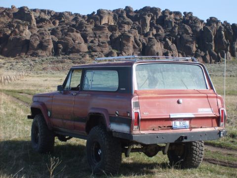 1989 Ford Bronco - A red SUV with a roof rack is parked in a field with a rocky landscape behind it.