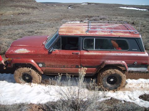 1989 Ford Bronco - This red Jeep Cherokee Chief is stuck in a muddy, snowy terrain, showing signs of wear and tear.