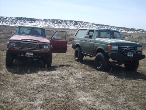 1989 Ford Bronco - A green 1989 Ford Bronco is parked next to a red Jeep Wagoneer in a dry, grassy field.