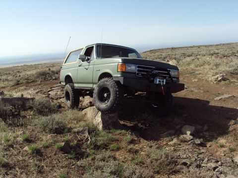 1989 Ford Bronco - A modified 1987 Ford Bronco navigates rocky terrain under a clear blue sky.