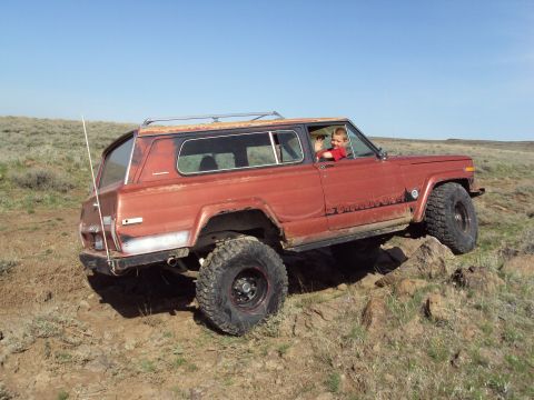 1989 Ford Bronco - A Jeep Cherokee Chief is shown off-roading on a rocky trail under a clear blue sky.