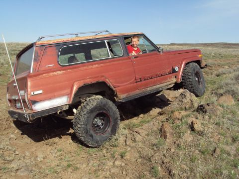 1989 Ford Bronco - A red Jeep Cherokee Chief navigates rocky terrain on a sunny day.