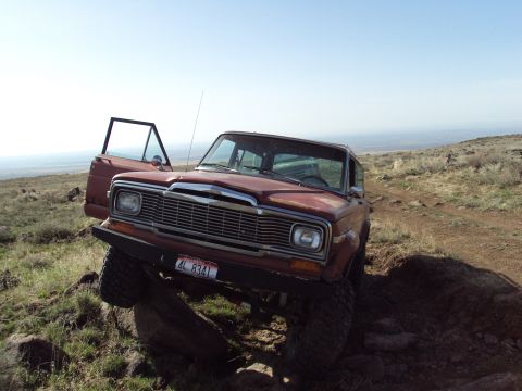 1989 Ford Bronco - Jeep Wagoneer navigating rocky terrain with its door ajar.