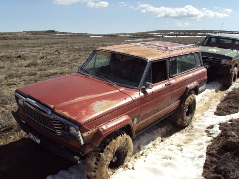 1989 Ford Bronco - Two off-road vehicles navigate a muddy and snowy trail, with the lead vehicle appearing to be stuck.