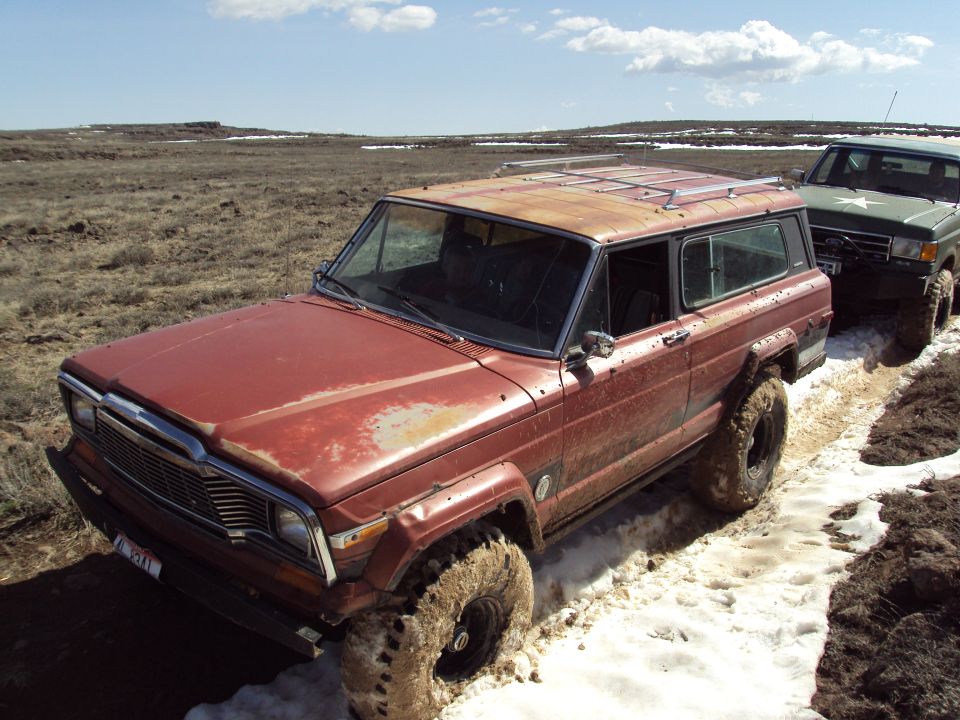Red Jeep Grand Wagoneer stuck in mud and snow, another vehicle behind it