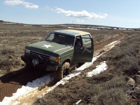 1989 Ford Bronco - A modified Ford Bronco navigates a muddy, snowy trail in a barren landscape.