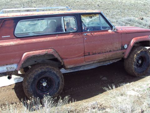 1989 Ford Bronco - This red SUV, identified by its "Cherokee" badging, is equipped with off-road tires and navigates a muddy trail.