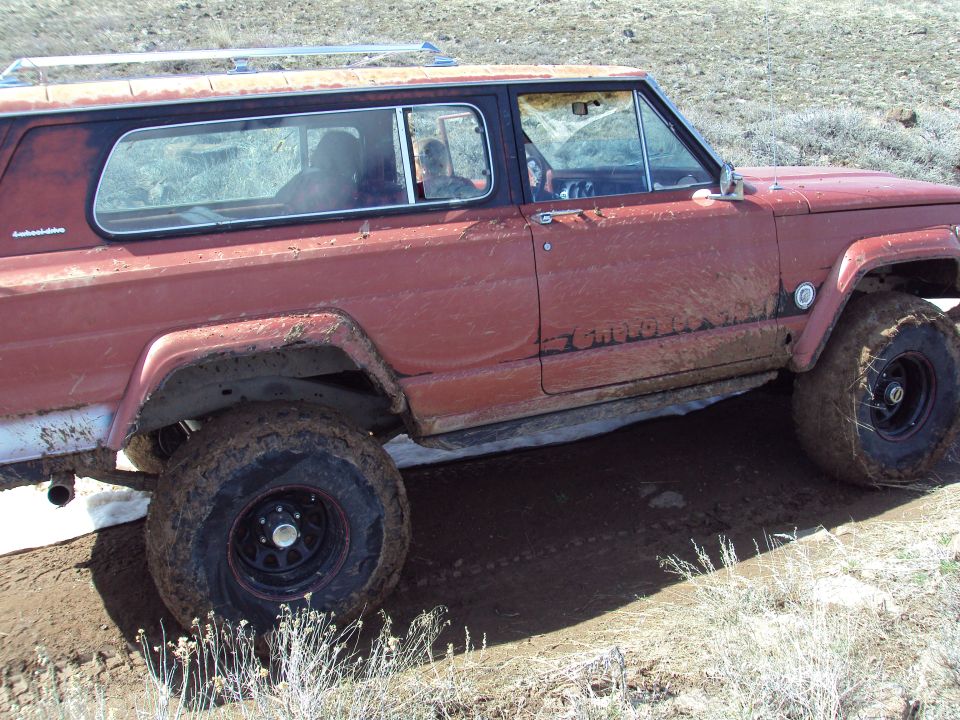 Red SUV with "Cherokee" badging on side, off-road tires, driving on muddy terrain