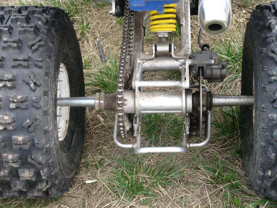 ATV rear axle with chain drive, yellow shock absorber, and knobby tires