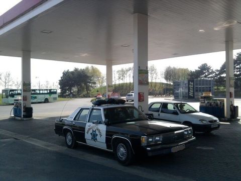 1991 Ford Crown Victoria - A 1991 Ford Crown Victoria police car is seen at a gas station, with another car and a bus in the background.