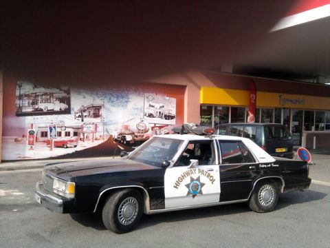 1991 Ford Crown Victoria - A black and white police car is parked in front of a Tiger Market store with a mural on the wall.