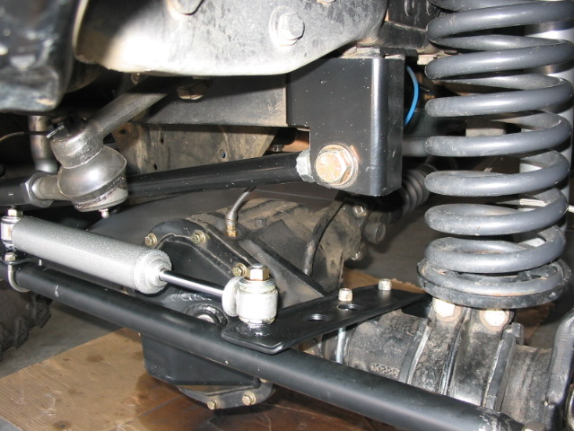 Underside view of front suspension with coil spring, tie rod, and steering stabilizer.
