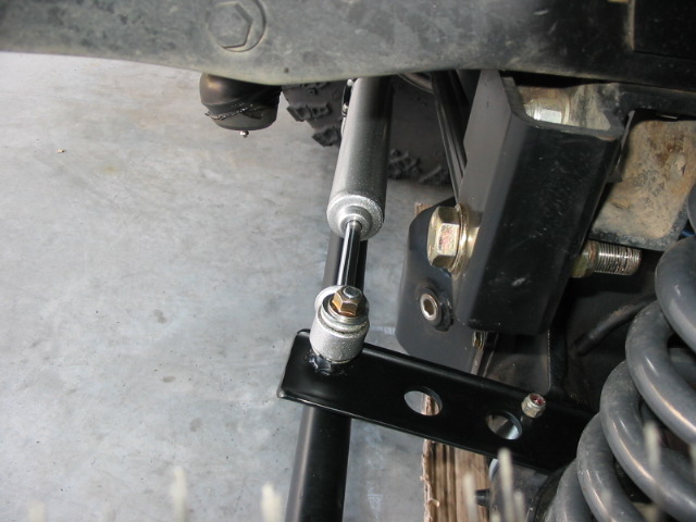 Steering stabilizer damper bolted to black bracket under a vehicle's front suspension