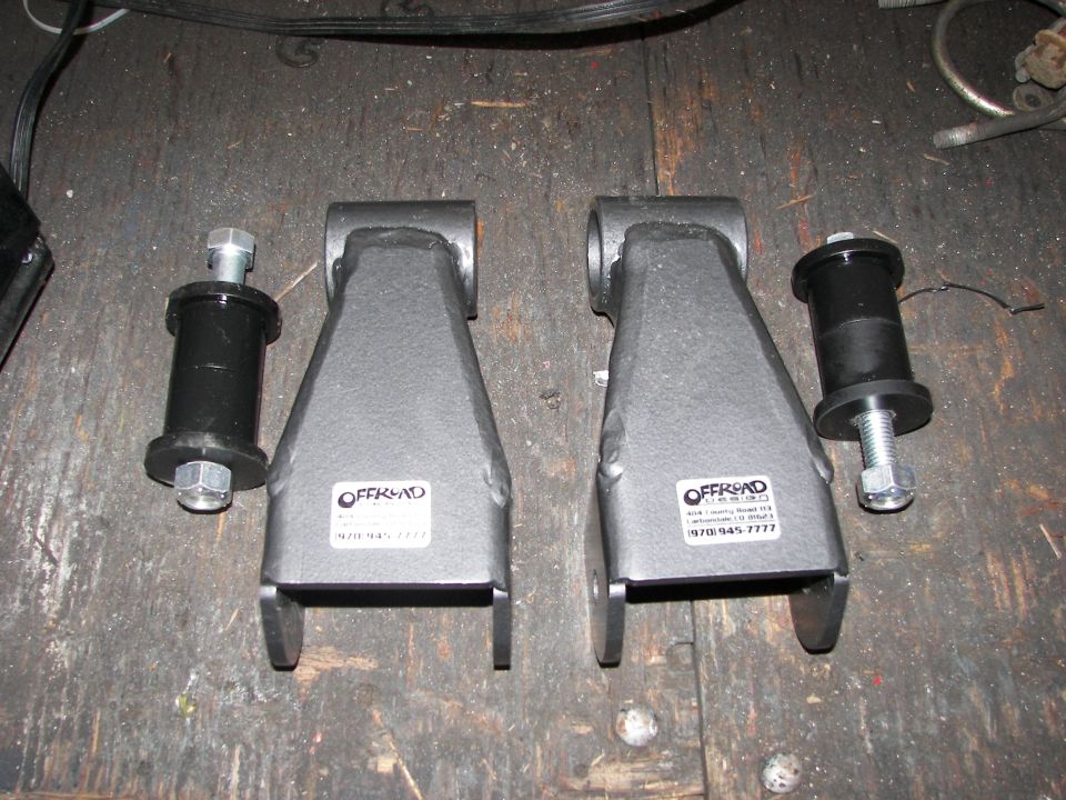 Pair of gray lift kit brackets with black bushings and bolts, labeled OFFROAD
