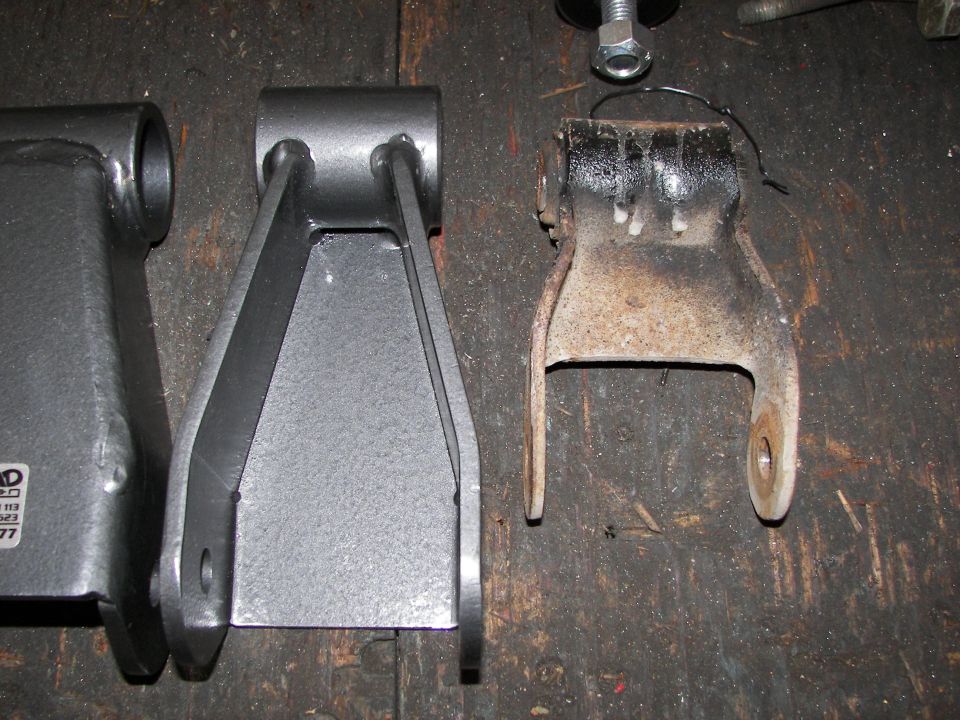 New gray suspension part next to a rusty old one on a wooden surface