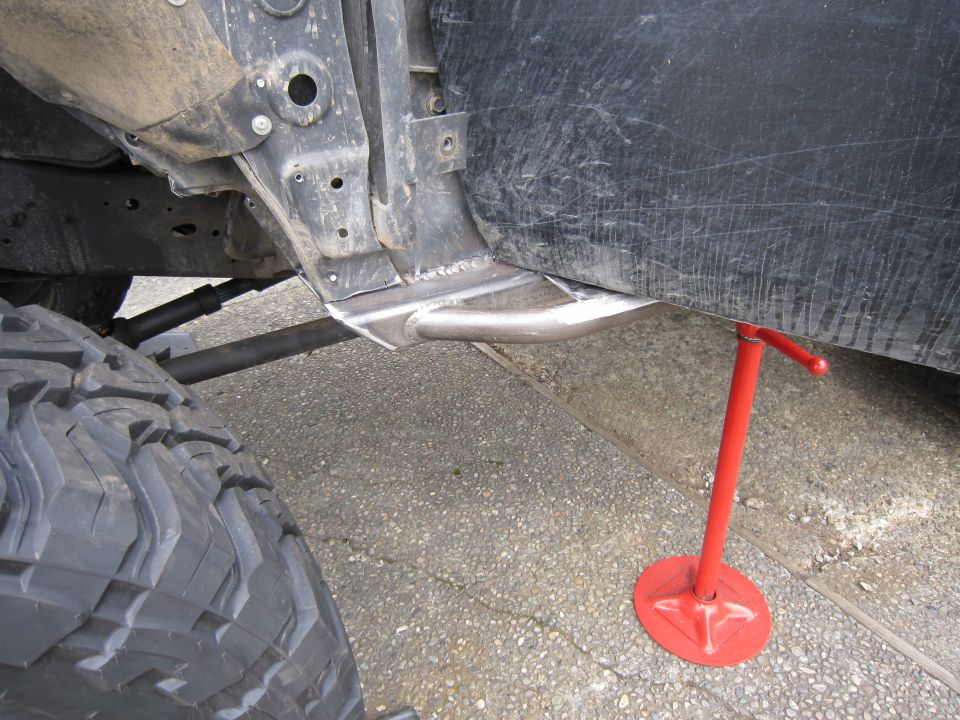 Close-up of a vehicle's rusty frame and large off-road tire, supported by a red jack