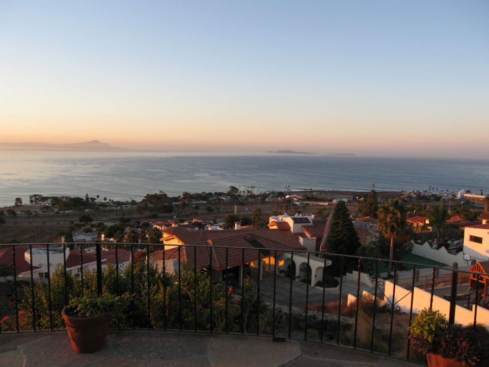 View of a coastal town and the ocean at sunset, with houses and palm trees in the foreground