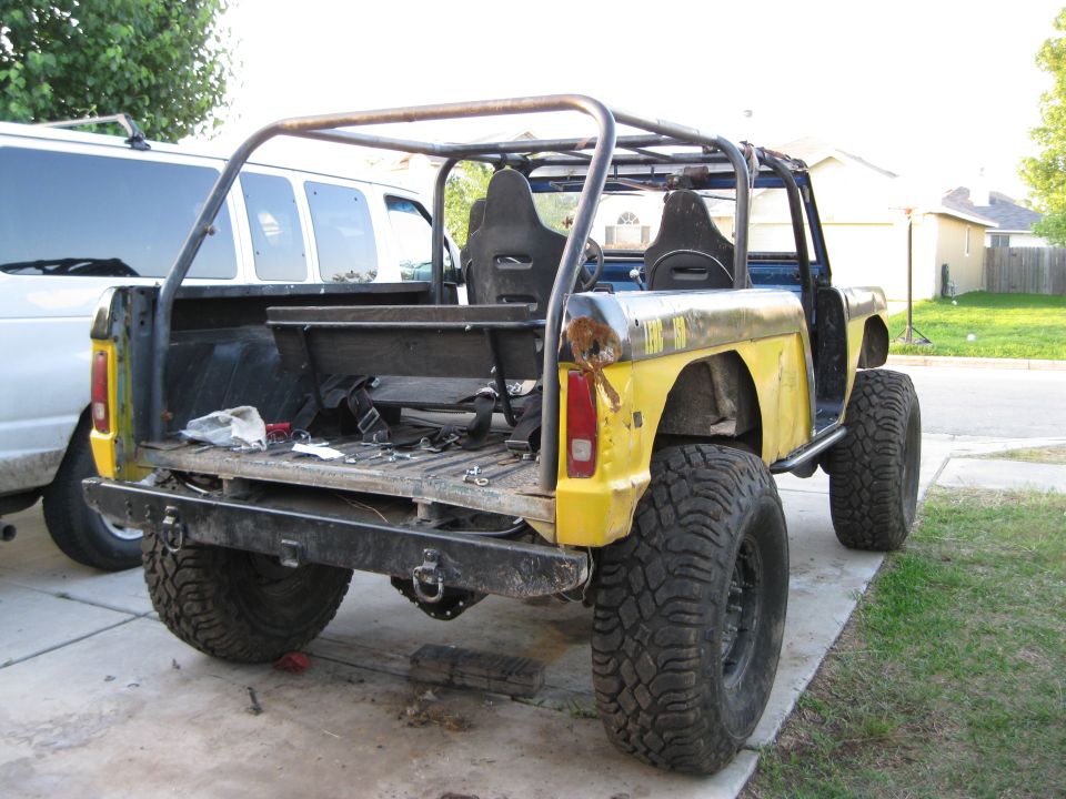 Yellow off-road vehicle with roll cage, aftermarket seats, and large tires, viewed from the rear