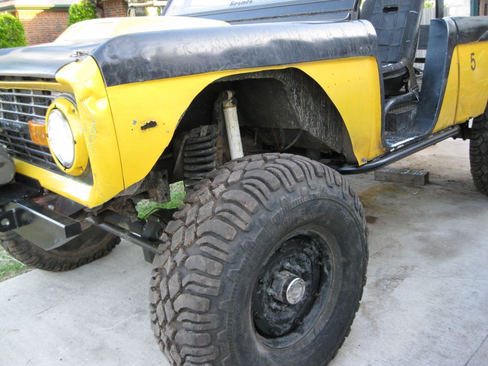 Yellow and black 1973 Ford Bronco with large off-road tires and a roll cage, viewed from the front 3/4 angle