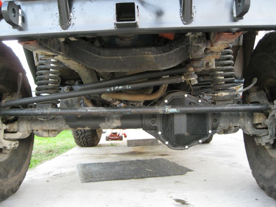 Underside view of a vehicle's suspension and differential. A red lawnmower is visible in the background