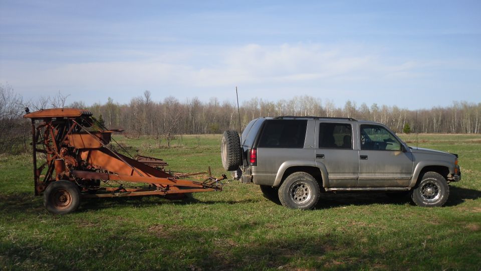 2000 Chevrolet Tahoe side view, towing an old orange farm implement in a grassy field