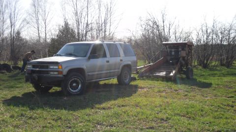 2000 Chevrolet Tahoe - A silver SUV tows a trailer with agricultural equipment in a grassy field.