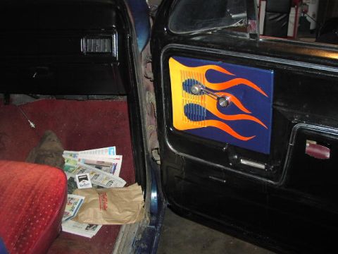 1981 Ford Bronco - The interior of a vehicle shows a custom door panel with a flame graphic and a vent, with papers scattered on the floor.