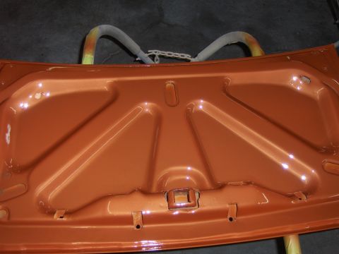 1980 Chevrolet Camaro - The underside of an orange car hood is shown, with visible support struts and a chain mechanism.