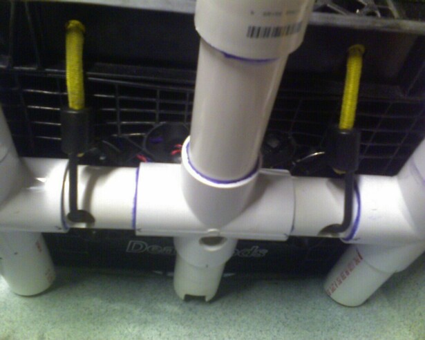 PVC pipe structure with yellow cords attached to black clips, resting on a black grate