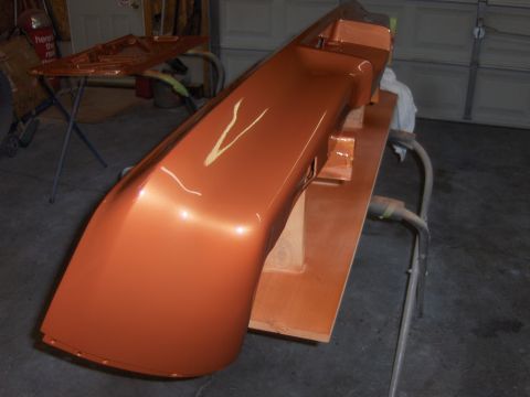 1980 Chevrolet Camaro - A freshly painted orange car bumper is mounted on a stand in a garage, ready for installation.