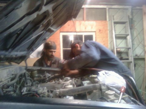 1985 Toyota Pickup/SR5 - Mechanics work on the engine of a truck with its hood open in a garage setting.
