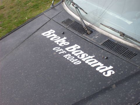 1985 Toyota Pickup/SR5 - The hood of a dusty truck displays "Broke Bastards OFF ROAD" decals, with windshield wipers in view.