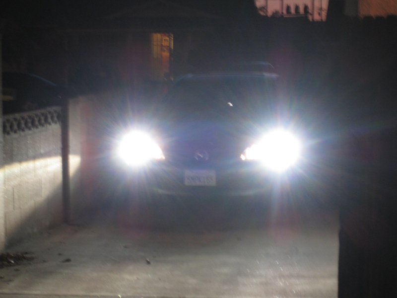 Front of a Mazda SUV with headlights on, parked in a driveway at night. License plate is visible