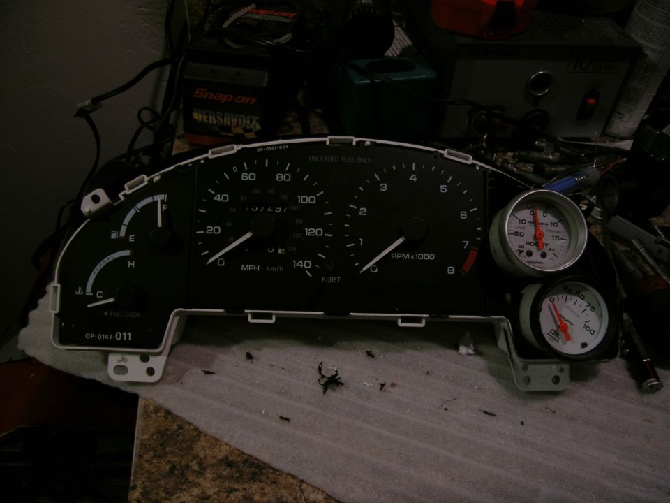 Car dashboard instrument cluster with speedometer, tachometer, fuel gauge, and two aftermarket gauges