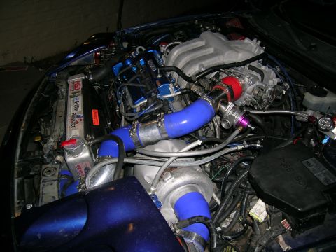 1995 Ford Probe - Custom turbocharged engine bay with prominent blue piping and a large turbocharger. The radiator has performance stickers.