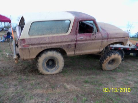 1978 Ford Bronco - A muddy 1978 Ford Bronco sits on a grassy field, its body showing signs of off-road use.