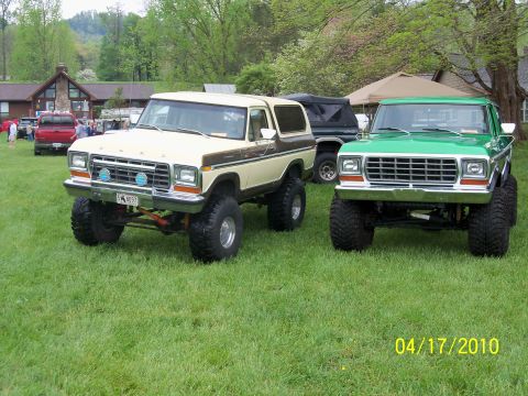 1979 Ford Bronco - Two lifted Ford Broncos from the 1970s are parked on a grassy field.