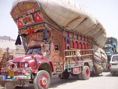 1995 Ford Bronco - A heavily adorned truck is parked alongside other vehicles, displaying intricate artwork and carrying a substantial cargo.