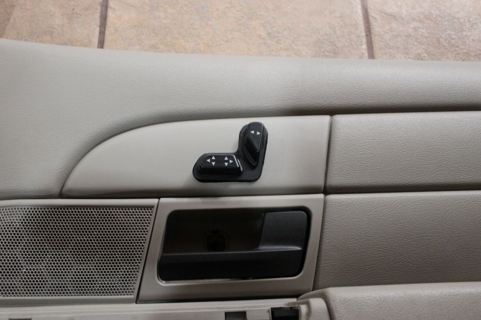 Close-up of black power seat switch and door release handle on a tan door trim panel