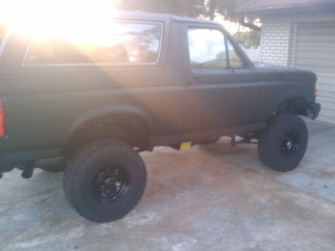 1993 Ford Bronco - This Ford Bronco is shown from the side, aftermarket wheels and tires, and a matte dark paint job.