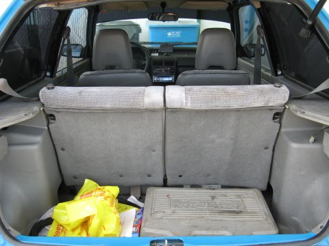 1991 Ford Festiva - The interior of a blue car, showing the trunk area with a yellow bag and a tool case, and the back seats visible.