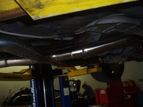 2002 Chevrolet Camaro - The underside of a vehicle with a dual exhaust system is shown on a lift, with a mechanic working in the background.